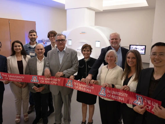 Group of individuals holding University of Arizona banners in front of an MRI machine.