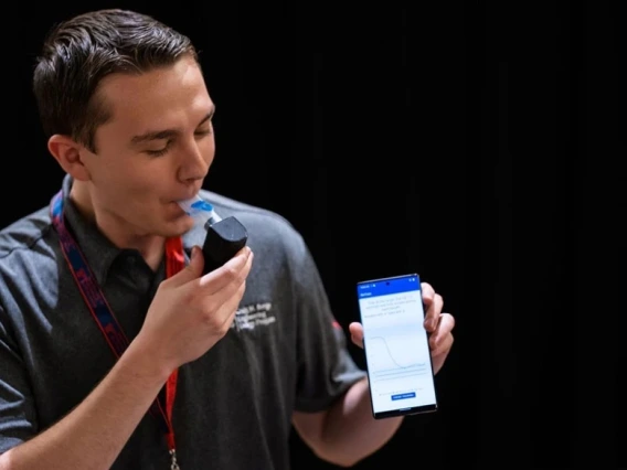 Person using a handheld breathalyzer device while holding a smartphone displaying the corresponding app's interface.