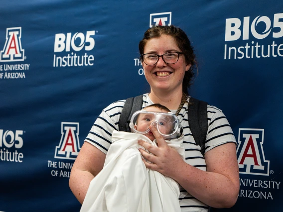 A mother with her baby who is dressed in a lab coat and safety goggles