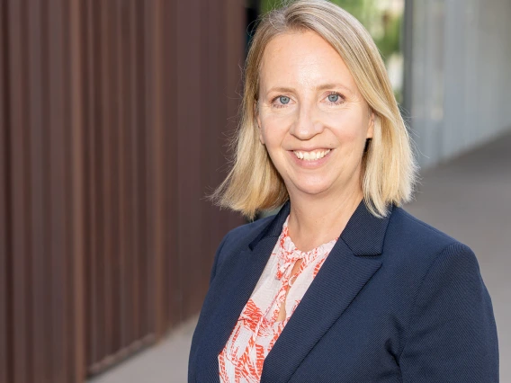 Portrait of a smiling person in a business suit, standing outdoors.