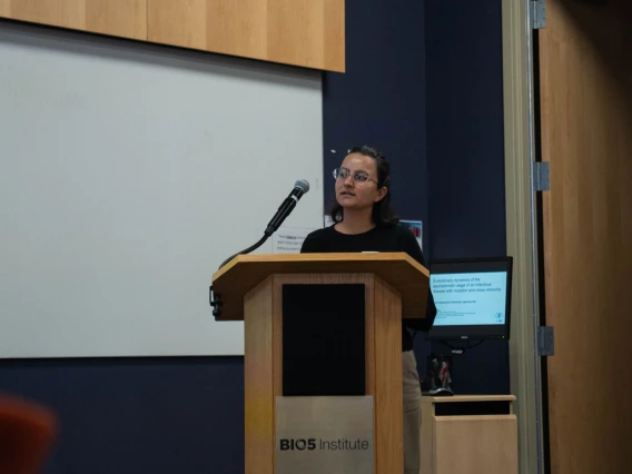 A person stands at a podium labeled "BIO5 Institute" in a lecture hall, facing an audience.