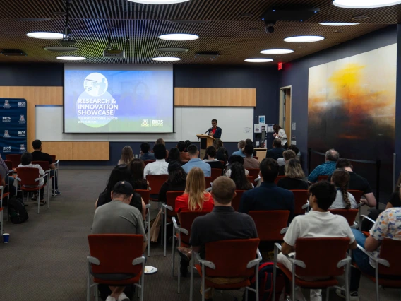 A person presenting at a Research and Innovation Showcase in a university auditorium filled with attentive audience members.