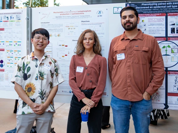 Three professionals standing in front of scientific posters at a conference, each wearing a name badge.