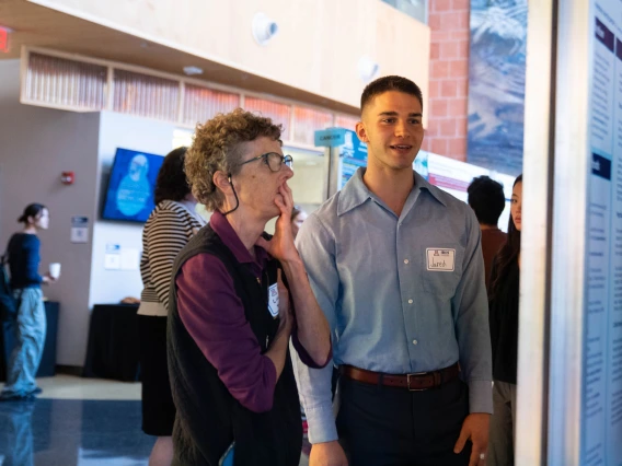 Two individuals engage in a discussion beside a poster presentation at a professional conference.