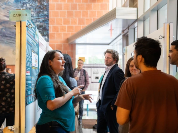 Individual presenting a research poster about cancer to a small group of attendees at a scientific conference.