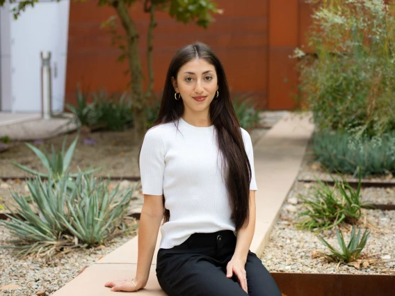 Person sitting on a concrete bench in a garden with various plants and a modern building in the background.