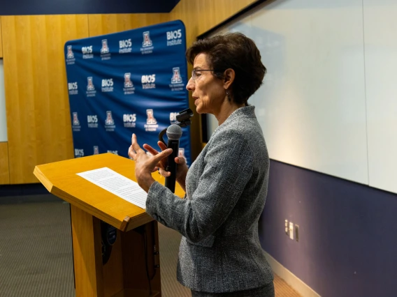 A person giving a speech at a podium with a microphone in a room with a "BIO5" banner in the background.