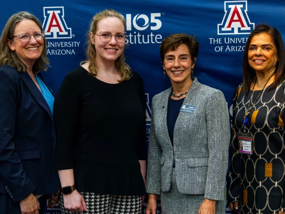 Four individuals posing at an event with banners for the University of Arizona and BIO5 Institute in the background.