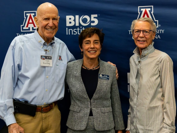 Three individuals standing together and smiling at a University of Arizona BIO5 Institute event, with banners of the institute and university visible in the background.