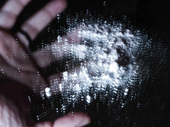A hand releasing a puff of fine powder against a dark background.