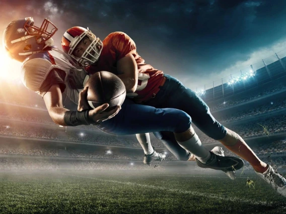 Two football players in a tackle during a night game at a stadium.