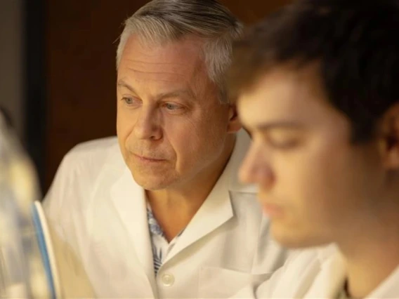 Two individuals in lab coats closely examining samples or screens in a laboratory setting.