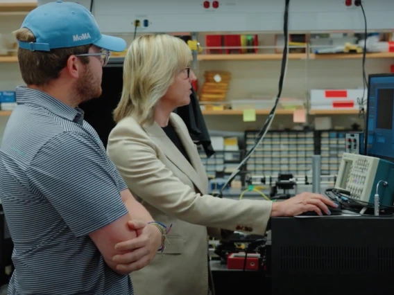 Two individuals are observing data on a computer screen in a tech lab setting.