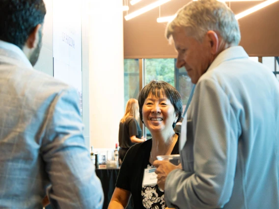 Three professionals conversing happily at a networking event, one of whom is wearing a name tag. The environment features modern architectural elements.