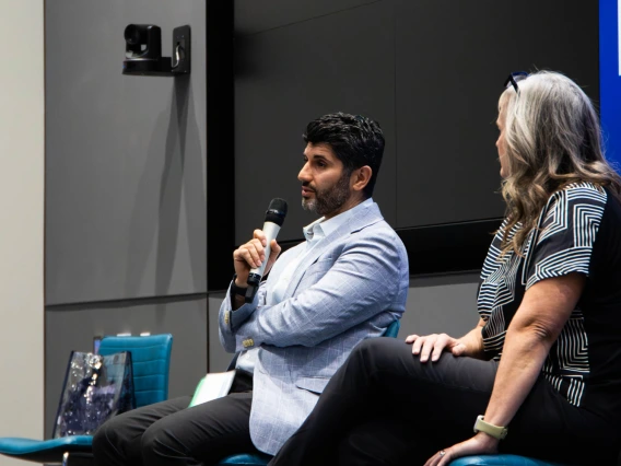 Two individuals sitting on a stage participating in a discussion, one holding a microphone.