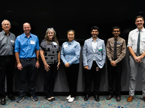 Group of seven professionals with name tags standing in front of a plain black background, smiling.