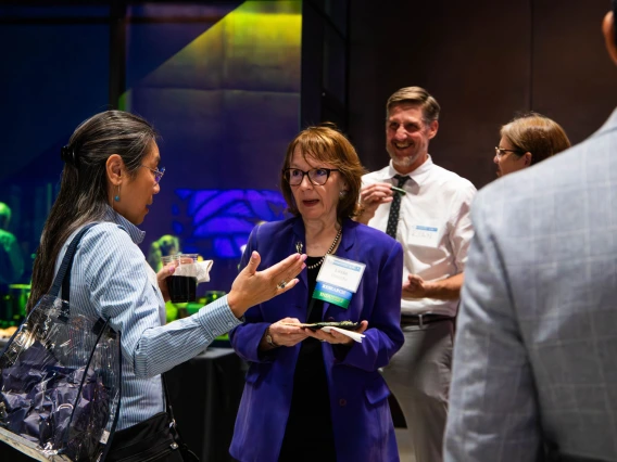 Group of professionals engaging in a conversation at a networking event, with one individual holding a plate of food and a business name tag visible.