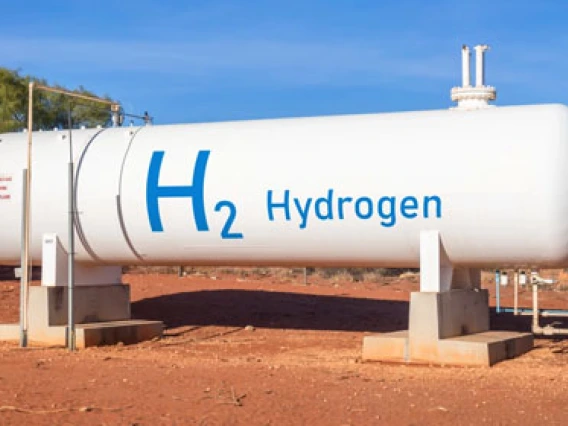 A large white storage tank labeled with "H2 Hydrogen" on a red dirt ground, supported by concrete blocks under a clear blue sky.