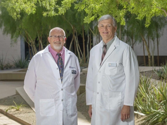 Two medical professionals in white lab coats standing outdoors, one with a badge labeled "Mayo Clinic."