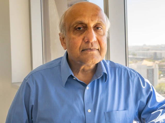 A man in a blue shirt is staring at the camera with the city view behind him.
