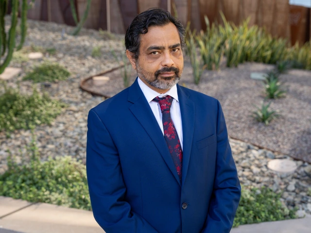 A man in a blue suit is staring at the camera. A desert scene is behind him.