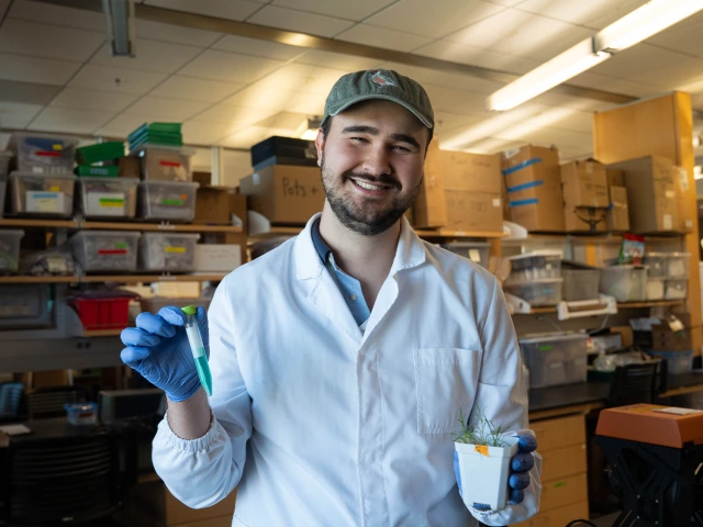 Man in lab gear holding a plant and green vial