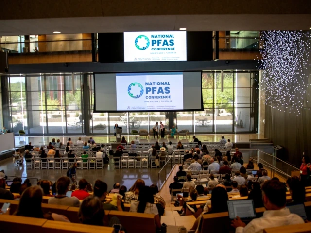 Group of people sitting in a large room with a screen that reads "PFAS"