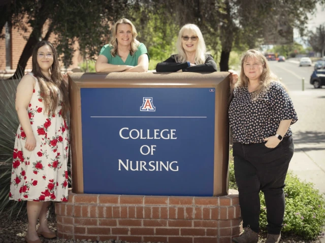 Four people stand outdoors beside a "College of Nursing" sign, which features the University of Arizona logo. 