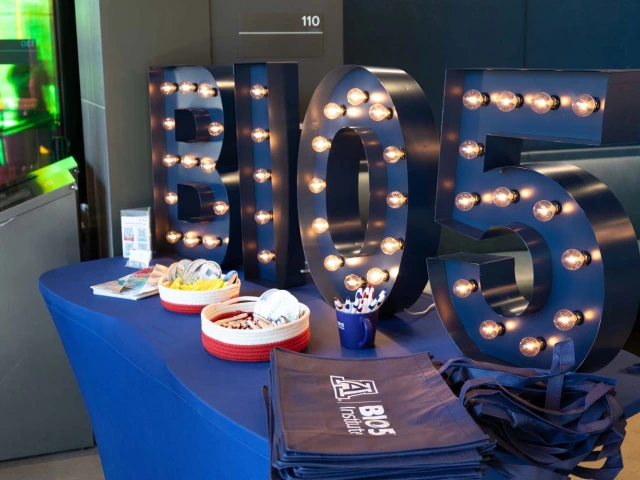 A table displays large illuminated letters spelling "BIO5." On the table are brochures, two baskets with items, a container with pens, and a stack of BIO5 Institute branded bags.