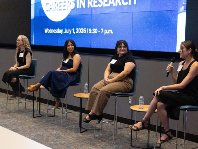 A panel discussion featuring four individuals seated in front of a large screen displaying the text "Careers in Research"