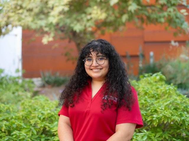 Person in a red shirt and dark curly hair against a green backdrop