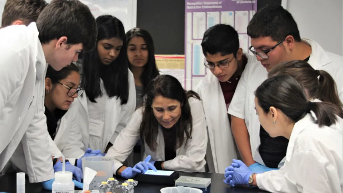 Group of students in lab coats gather around a scientist