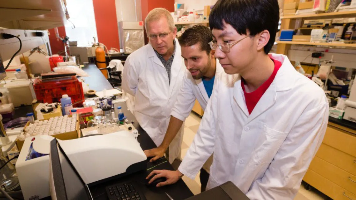 Student in lab coat works at a machine in laboratory
