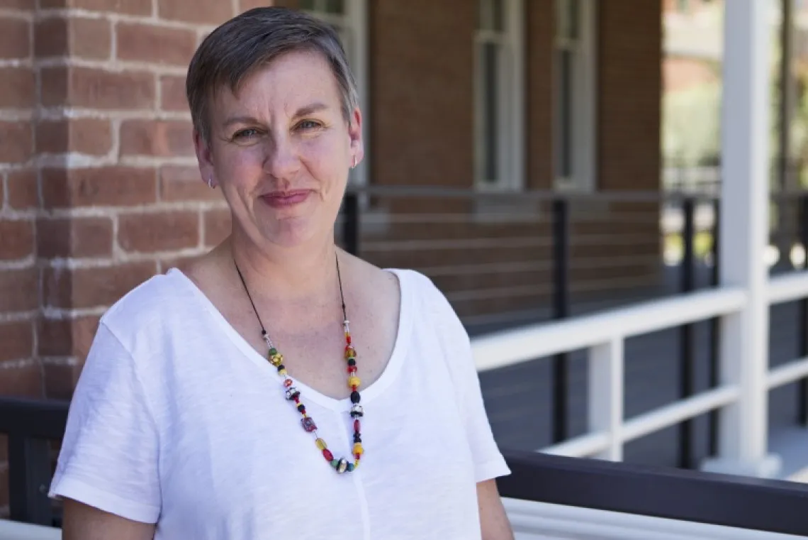 Short-haired woman with a colorful beaded necklace and wearing a white shirt