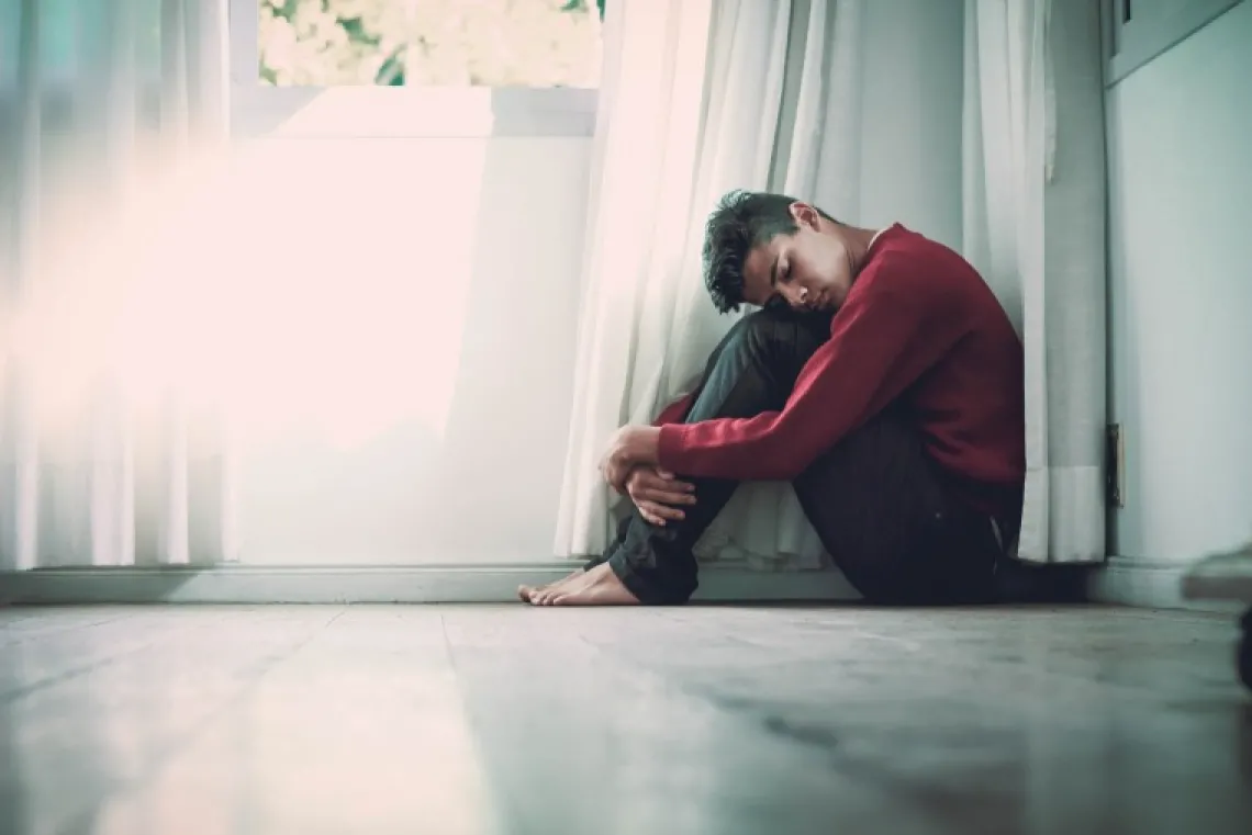 Person sitting on the ground hugging their knees looking sad