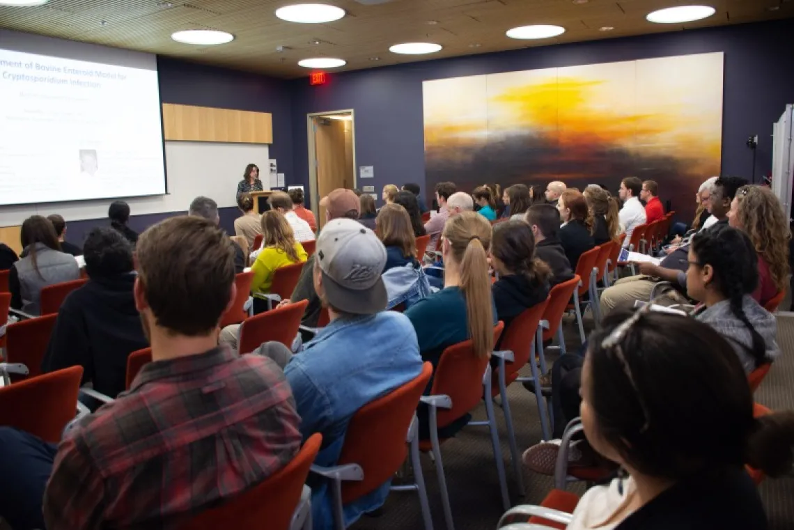 Crowd listens to a person presenting research at a podium