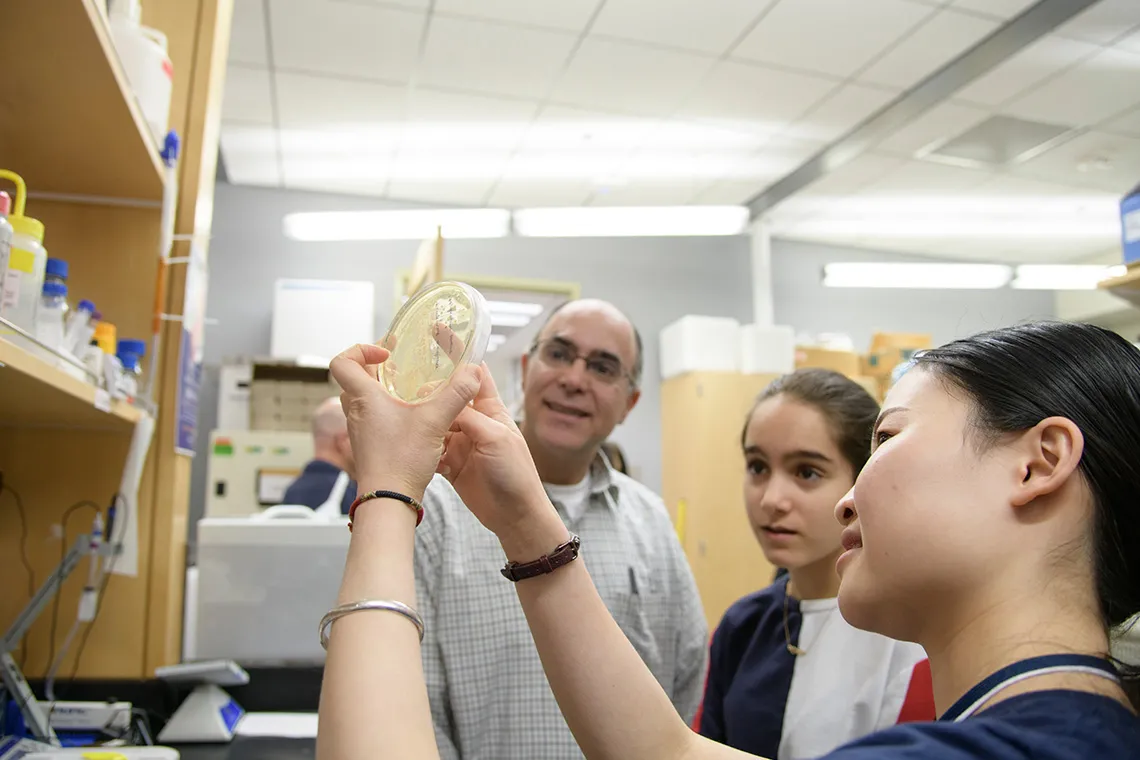 a researcher holding a petri dish explaining it contents to a group of people