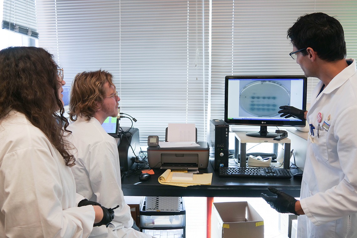 A researcher pointing at samples on a computer with 2 students