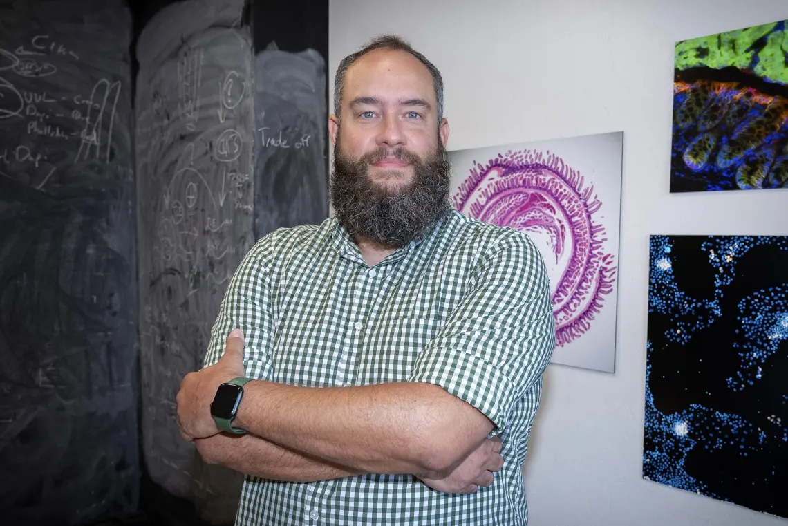 Person standing with arms crossed in front of a blackboard with chalk drawings and colorful scientific images on the wall.