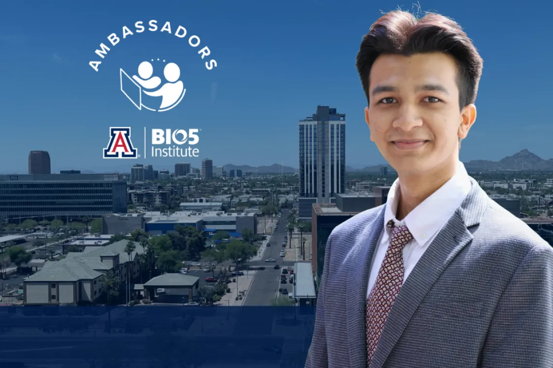 Professional portrait of an individual with short hair, wearing a suit, standing in front of a cityscape with the 'Ambassadors' logo, the University of Arizona (UA) emblem, and the BIO5 Institute logo visible in the background.