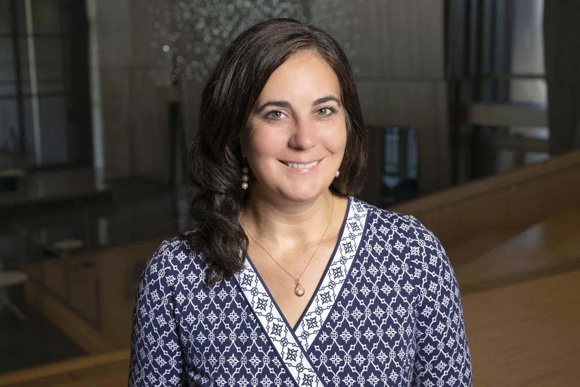 A person smiling in front of a darker background, whit a blue and white design shirt