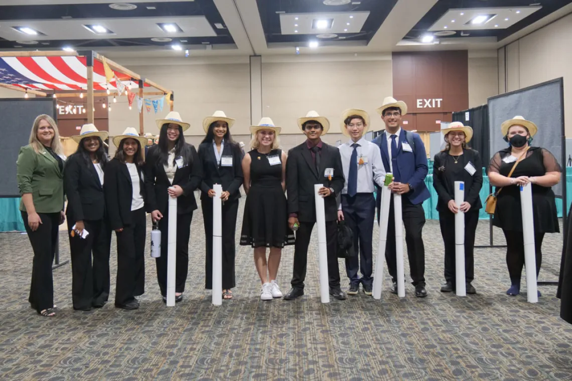 Students posing with their rolled up scientific posters wearing cowboy hats