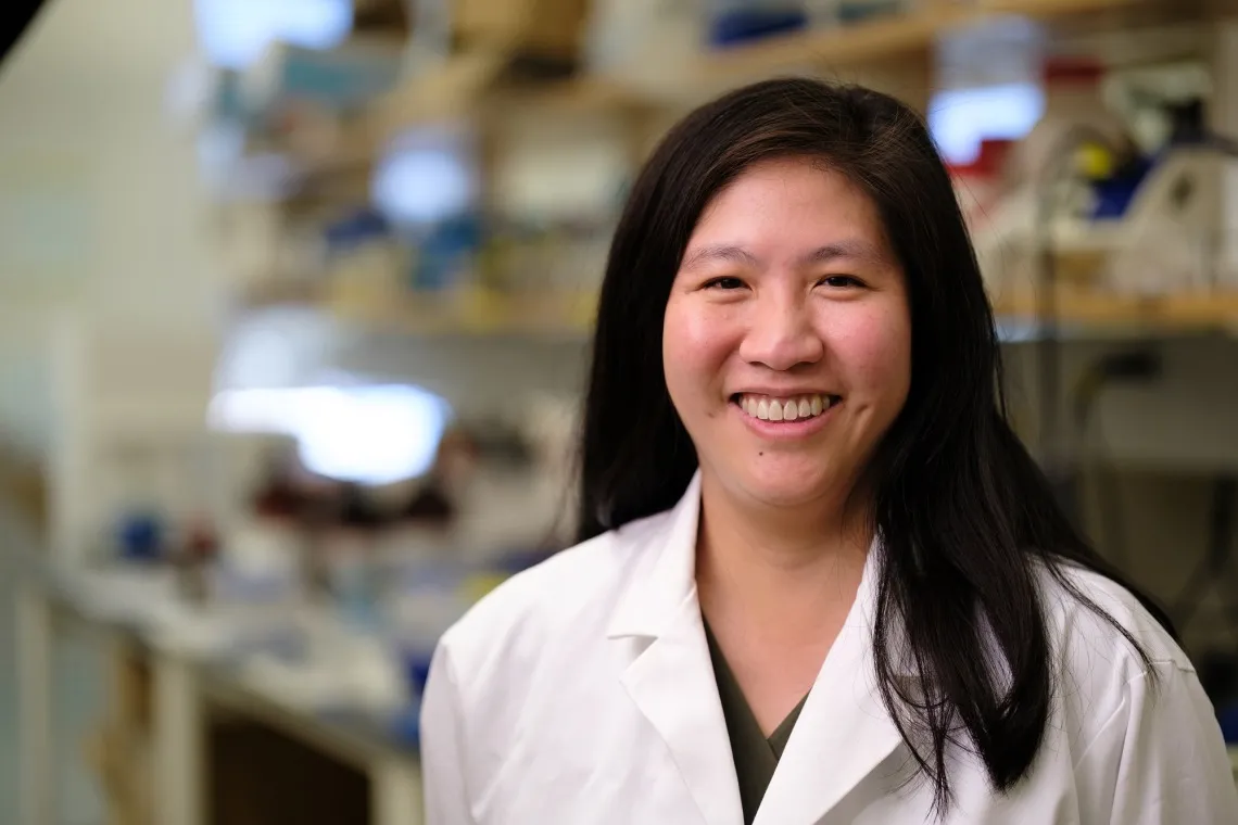 Person wearing a white lab coat smiling in a laboratory environment.