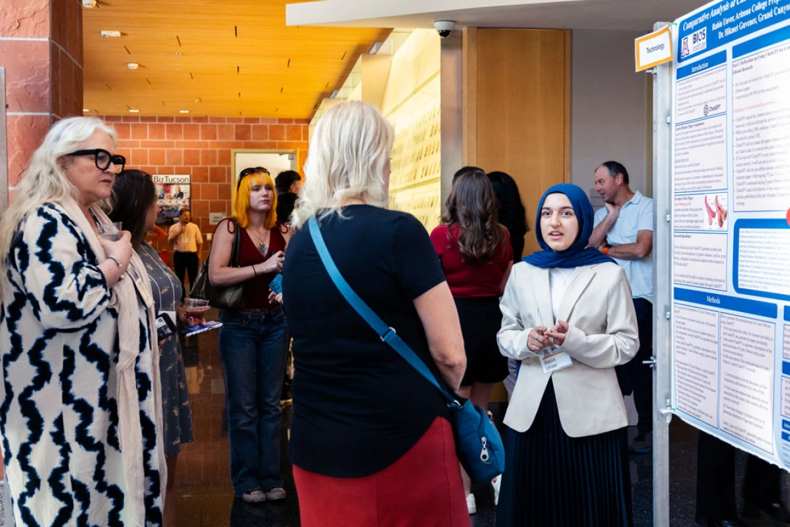 People conversing at a conference near informational posters, with one person wearing a hijab.