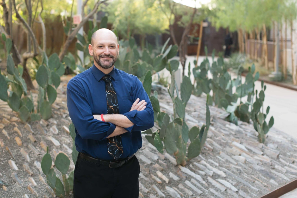 Person in a business casual outfit standing with crossed arms in front of a cactus garden.