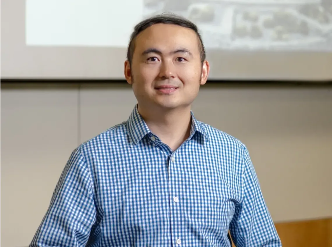 Image of Jianqin Lu smirking with blue collard shirt and whiteboard in background. 