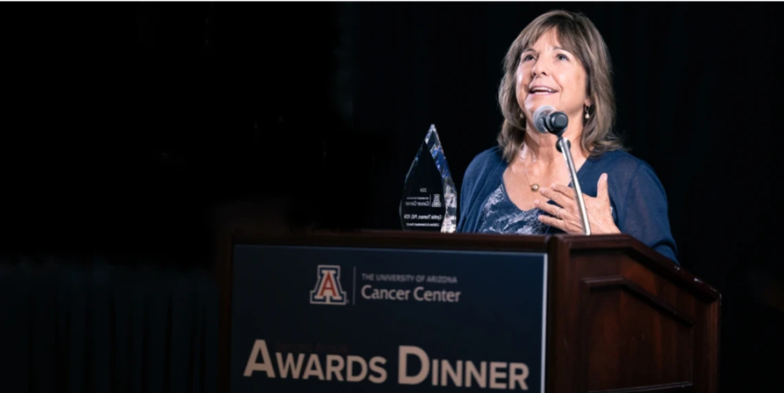 Person accepting an award at the University of Arizona Cancer Center Awards Dinner, standing at a podium with the event name visible.