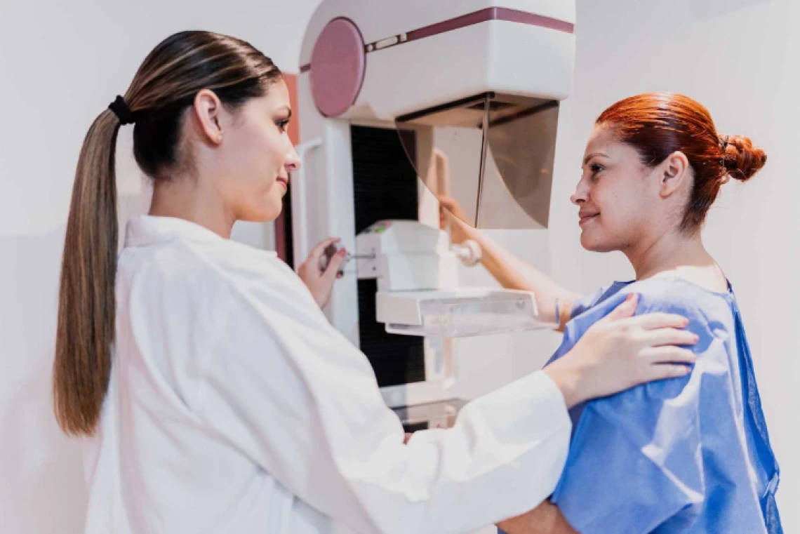 A medical professional assists a patient with a mammogram examination in a clinic.