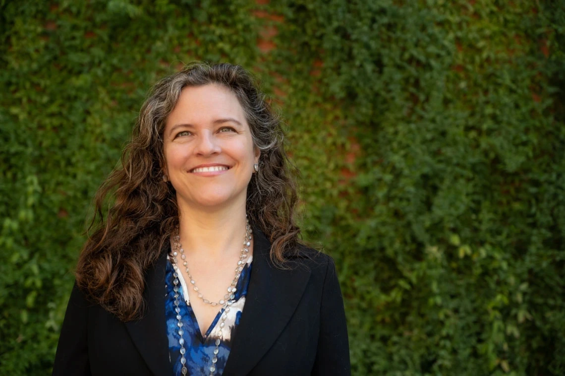 Person smiling in front of a lush green ivy-covered wall.