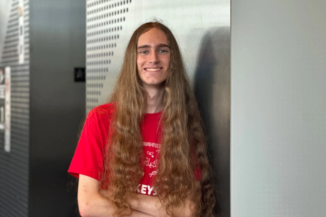 Young man with long hair wearing a red shirt stands confidently with his arms crossed